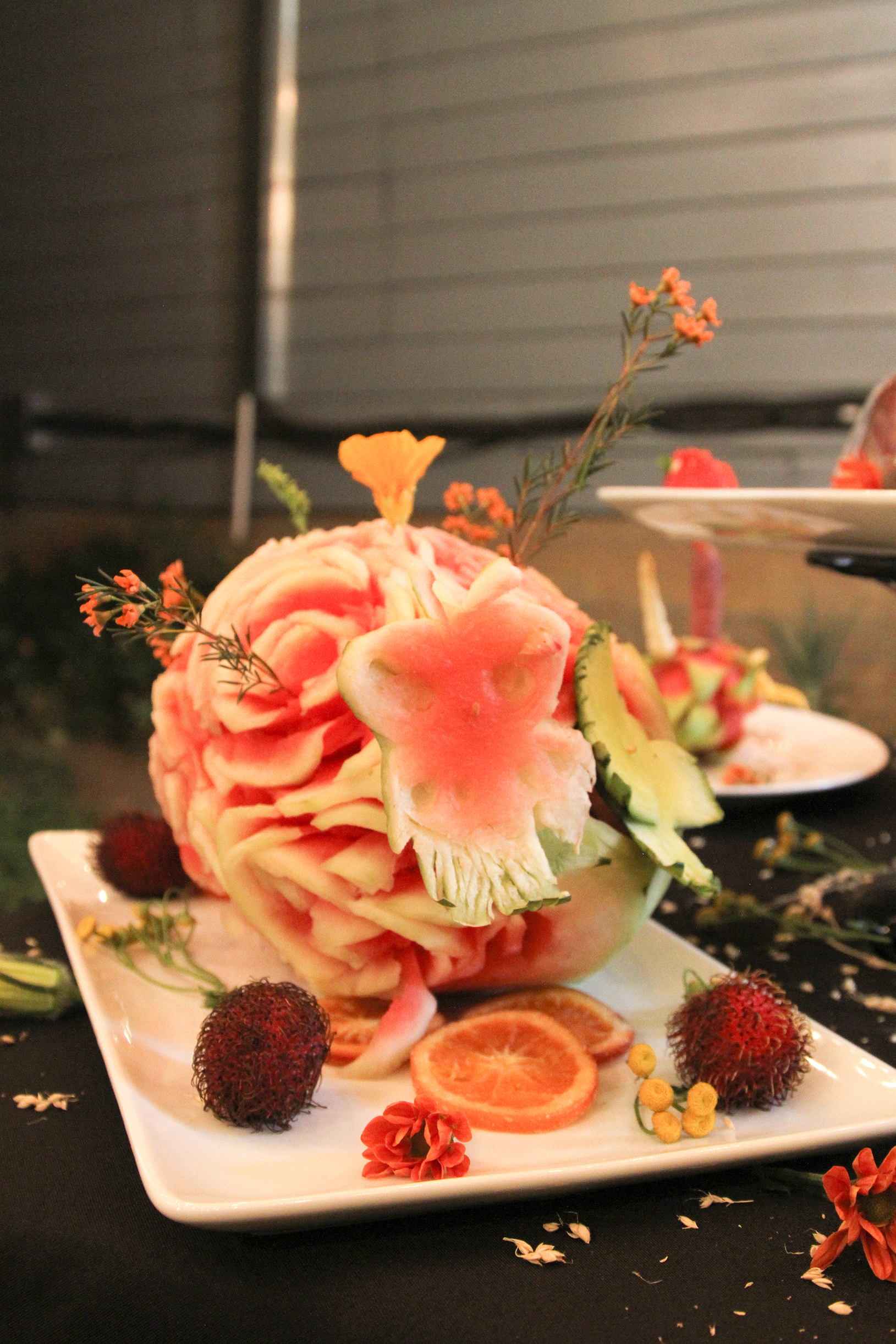 A watermellon carved with flower patterns surrounded by fruit on a white plate